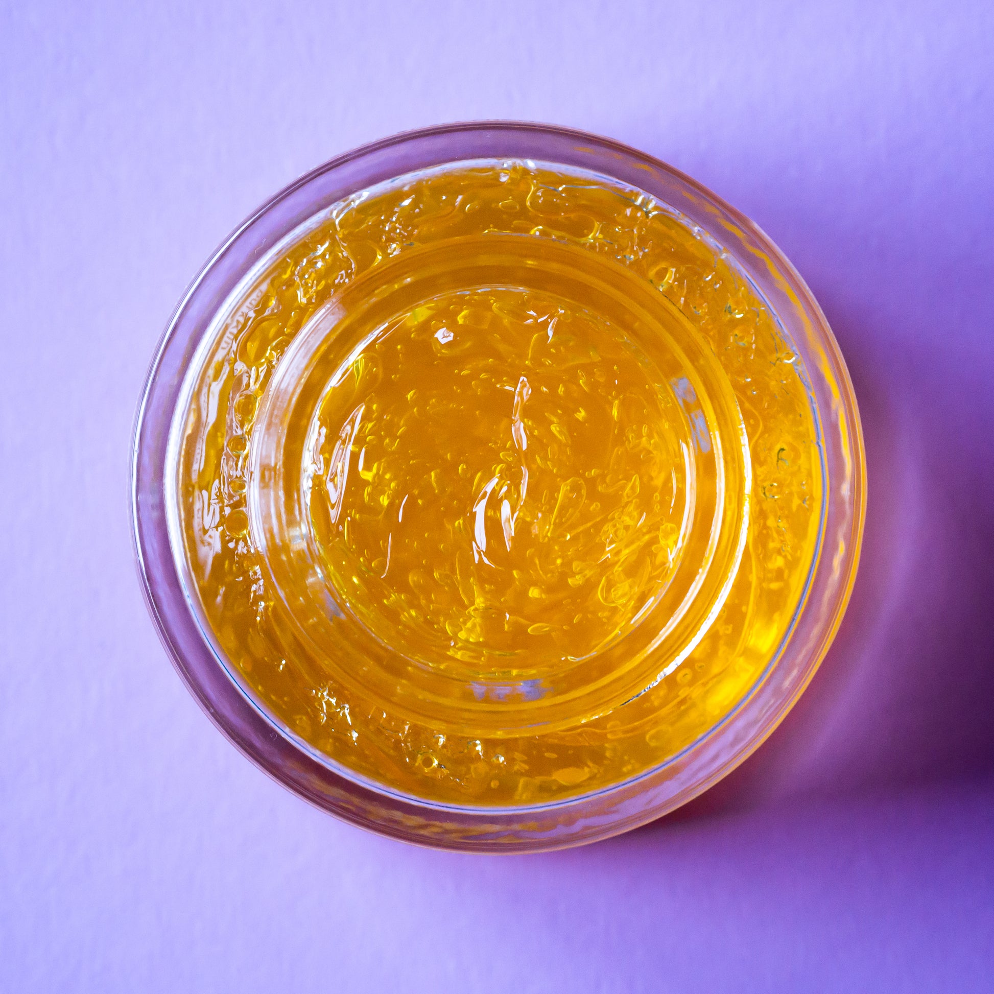 Clear container with yellowish gel-like substance on a purple background