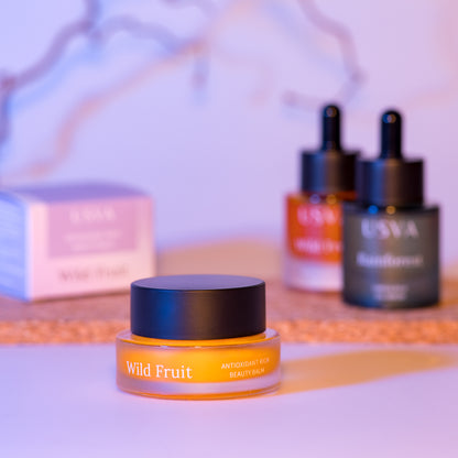 Orange skincare product with black cap labeled 'Wild Fruit' on a blurred background with skincare bottles.
