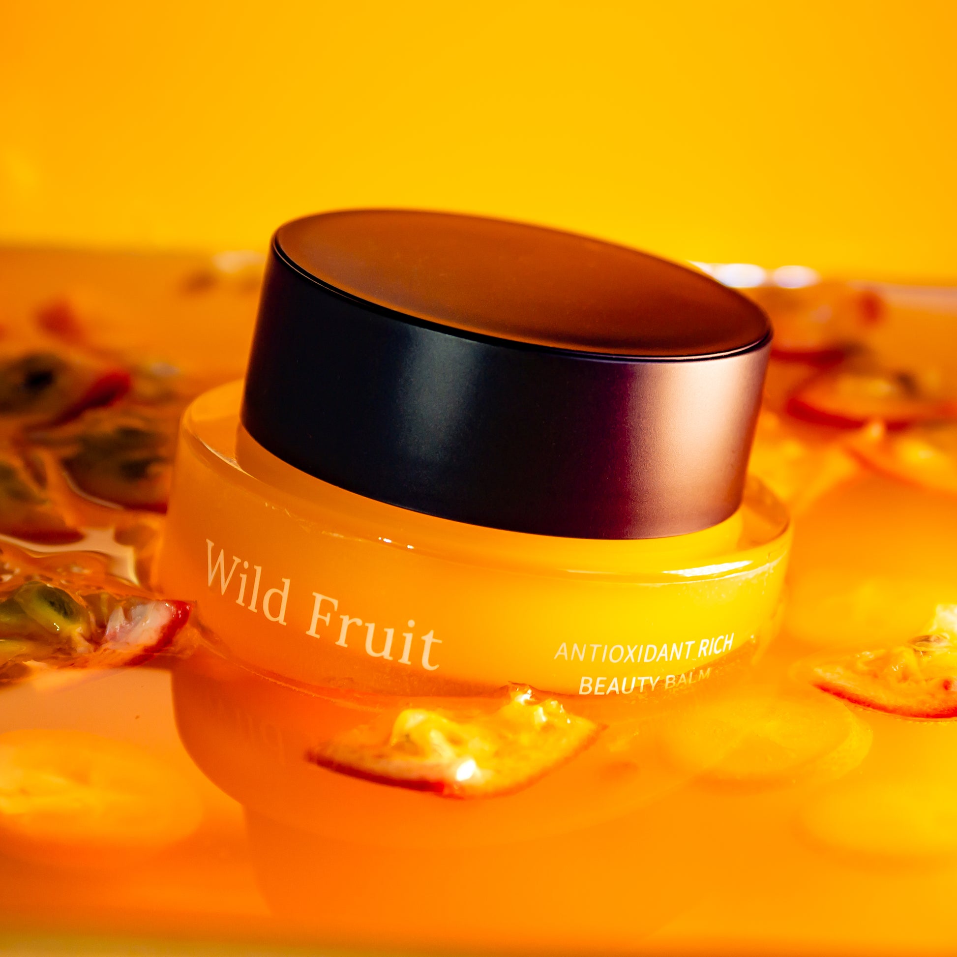Jar of 'Wild Fruit' beauty balm with a black lid on an orange background